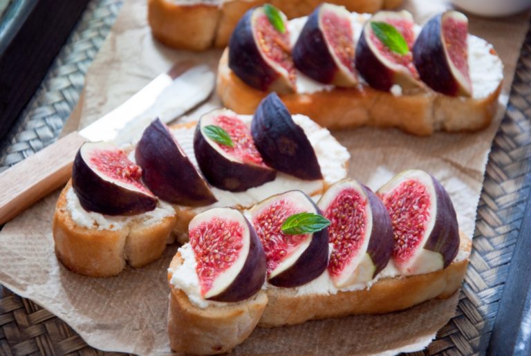 sliced figs and ricotta on baguette slices topped with basil