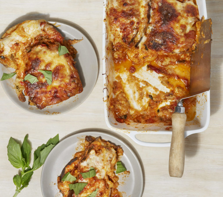 eggplant parm in a baking dish with two plates of the dish