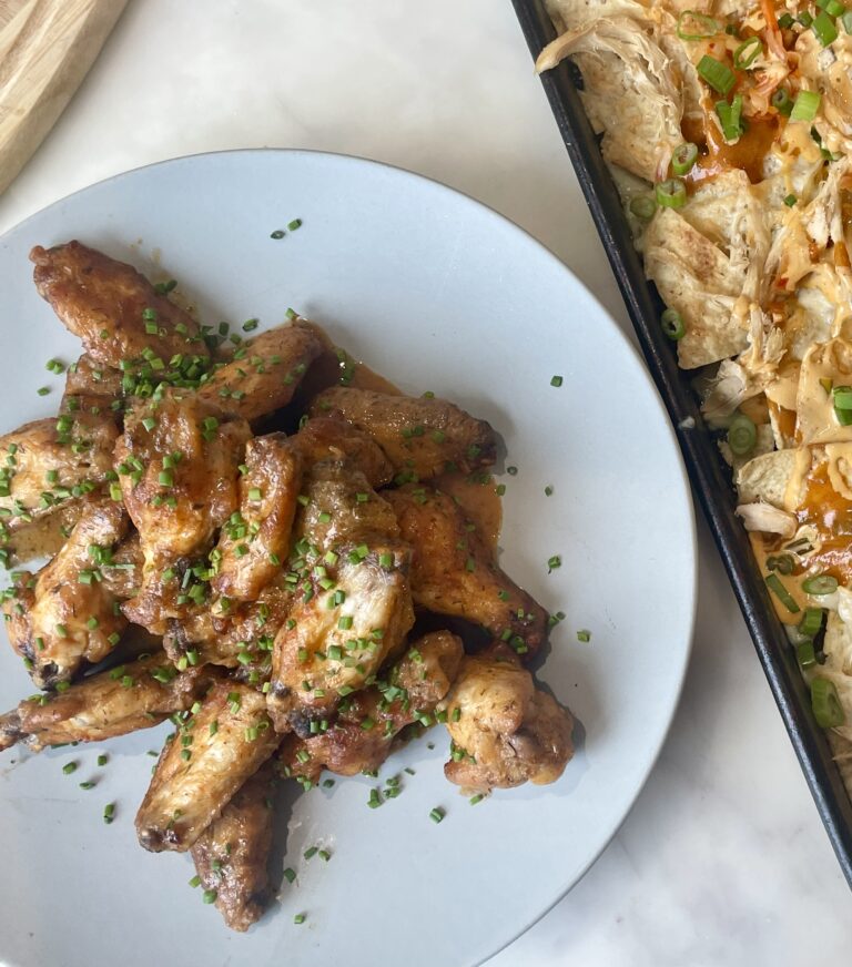 chicken wings on a plate next to a sheet pan of nachos